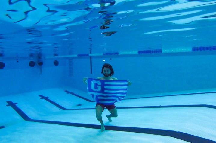 Student under water in a swimming pool holding a ֱ Flag